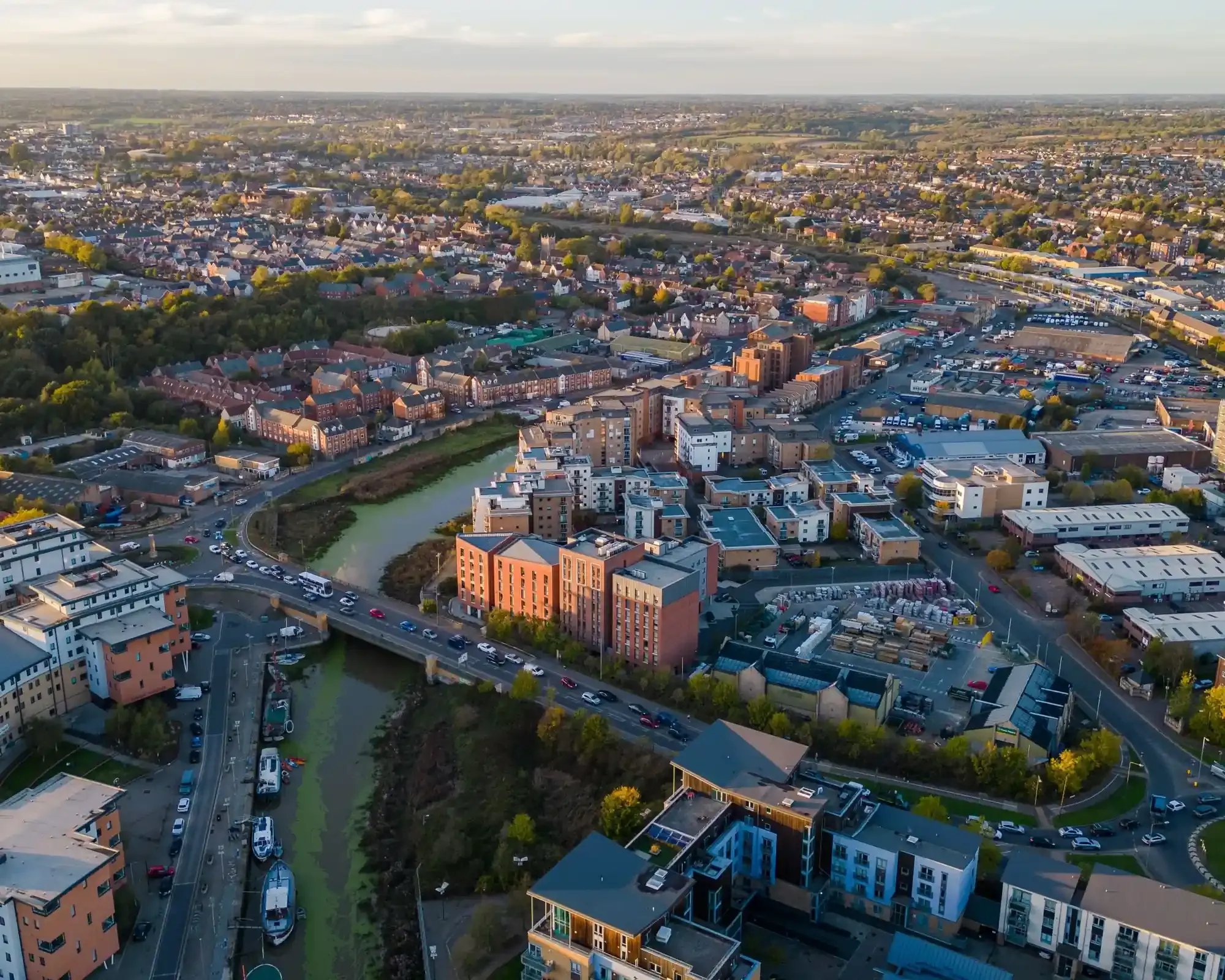 Aerial view of the Hythe in Colchester at sunset, with apartment blocks and moored boats along the River Colne and the city stretching into the distance.