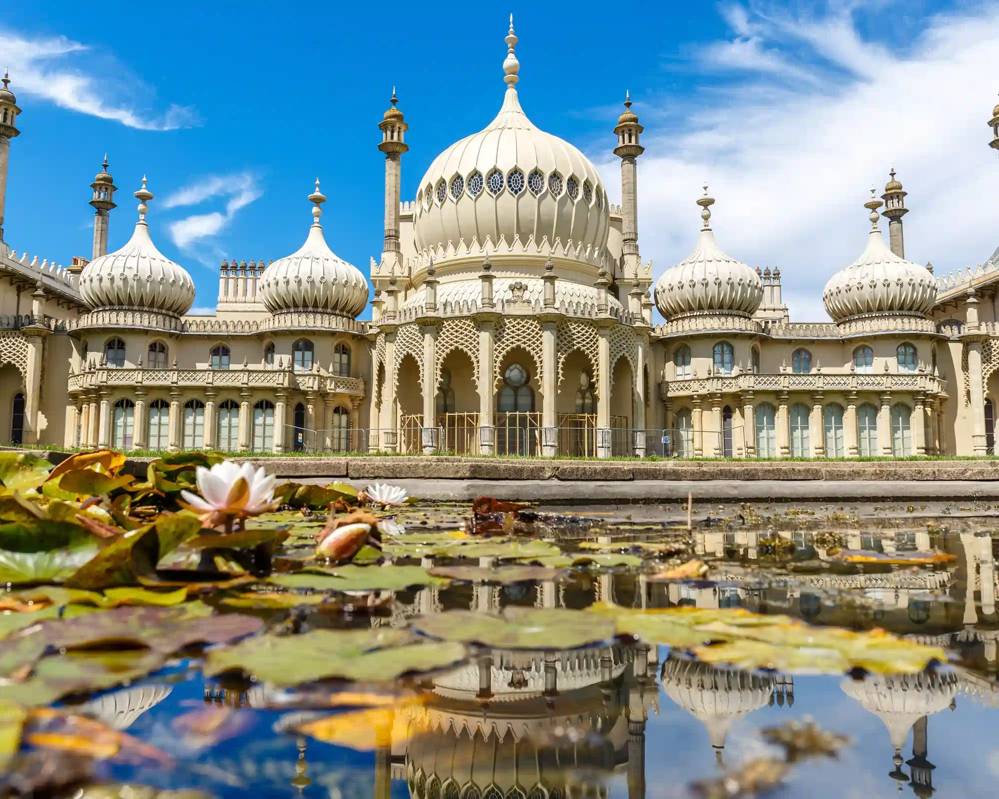 The Royal Pavilion in Brighton, with its cream onion domes and minarets reflected in a lily pond under a bright blue sky.