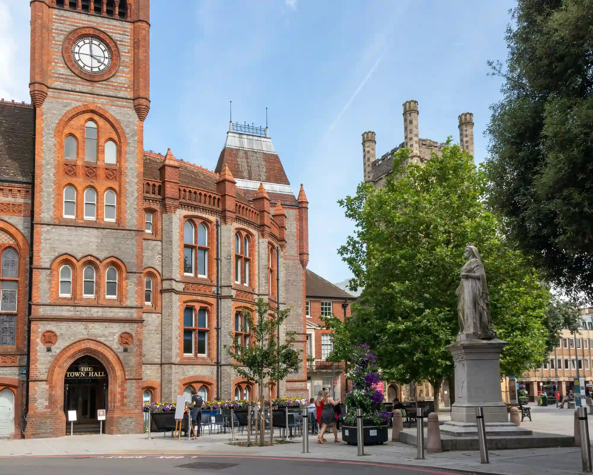 Reading Town Hall's red and grey brick Victorian clock tower, with a statue of Queen Victoria and the tower of St Laurence's Church in the square beside it.