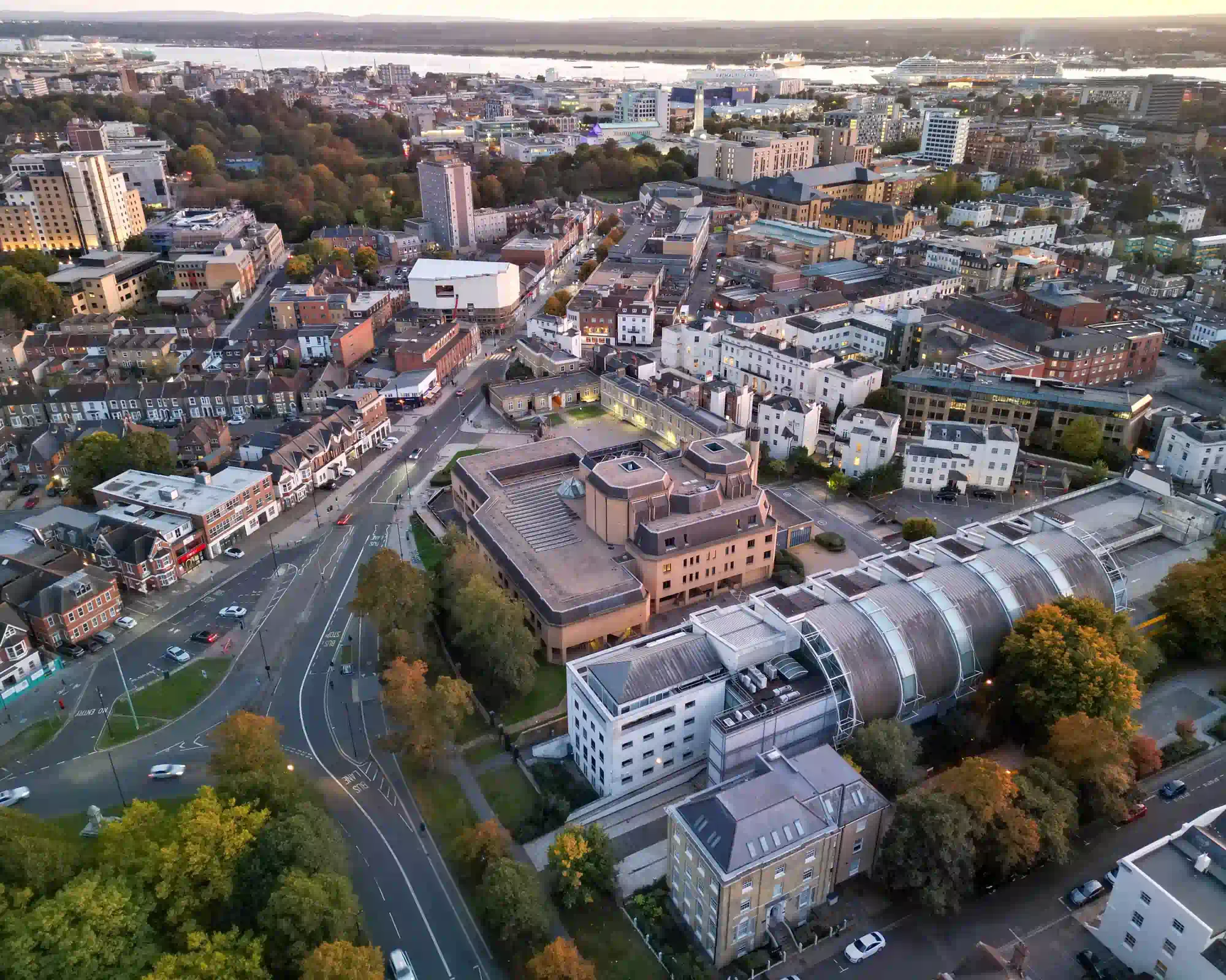 Aerial view of Southampton at dusk, with autumn trees and city centre streets leading towards the docks, where cruise ships are moored on Southampton Water.
