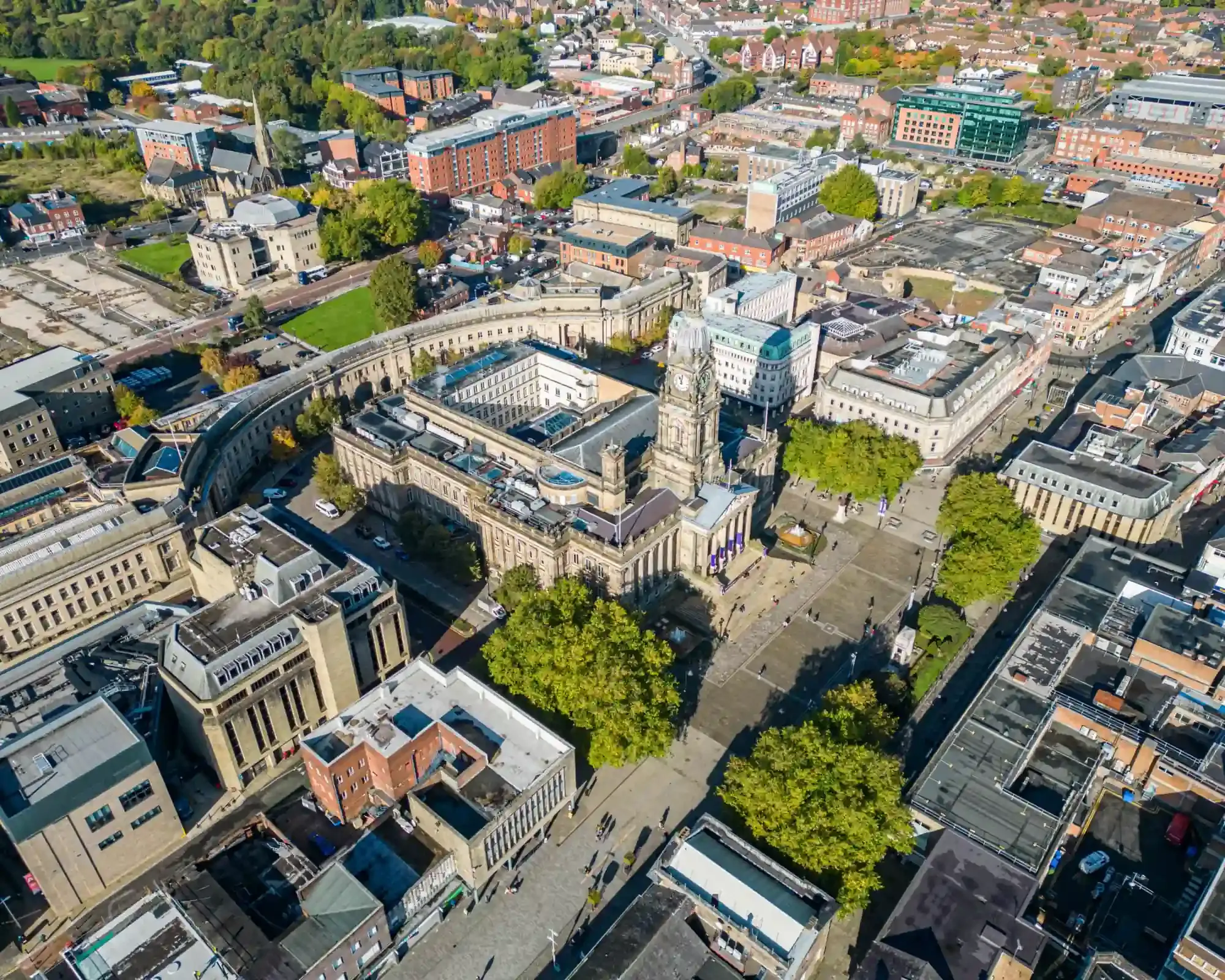 Aerial view of Bolton town centre showing the Town Hall clock tower, its curved crescent of civic buildings and the tree-lined Victoria Square.