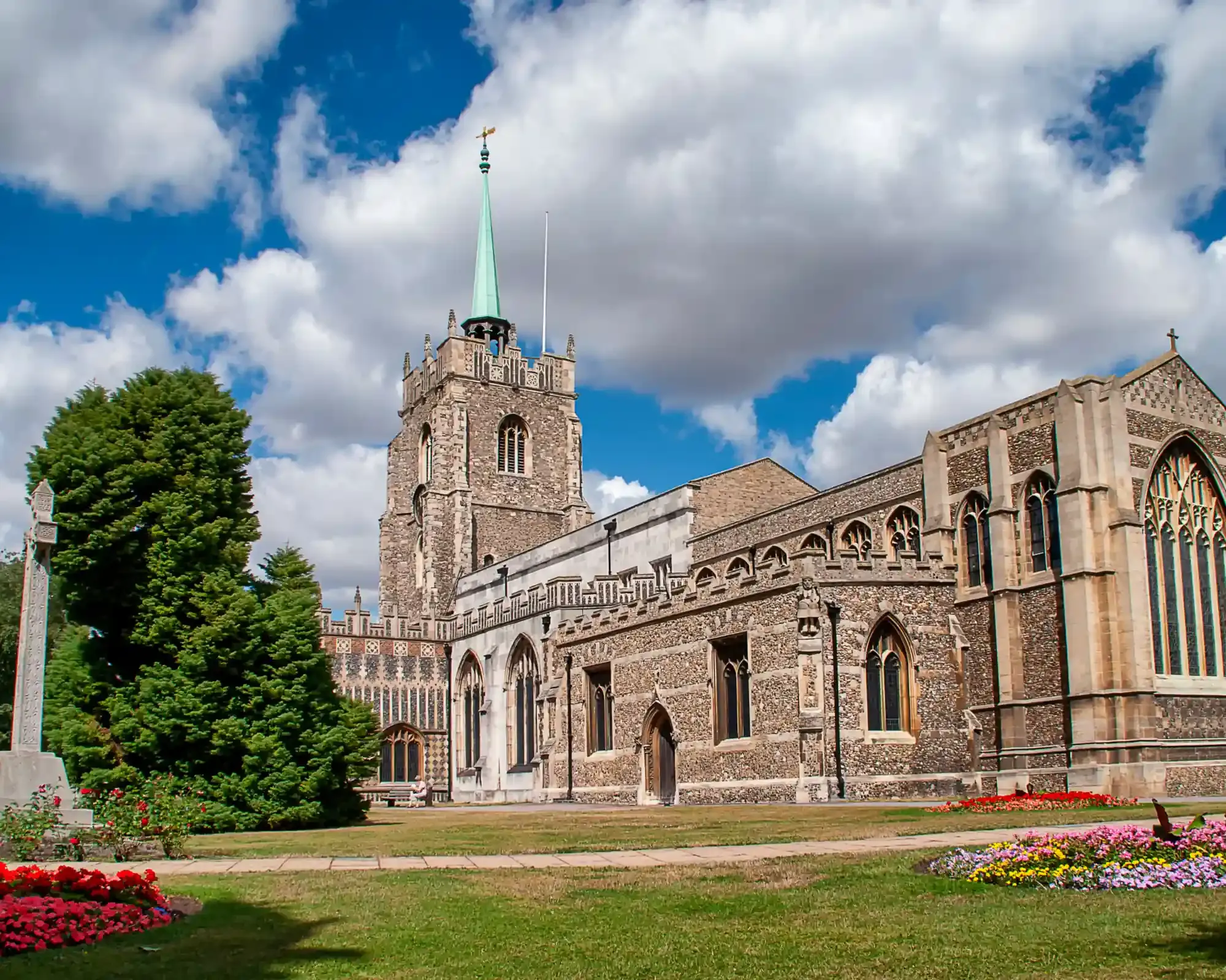 Chelmsford Cathedral's flint tower and green copper spire above the cathedral gardens and flower beds in Chelmsford city centre.