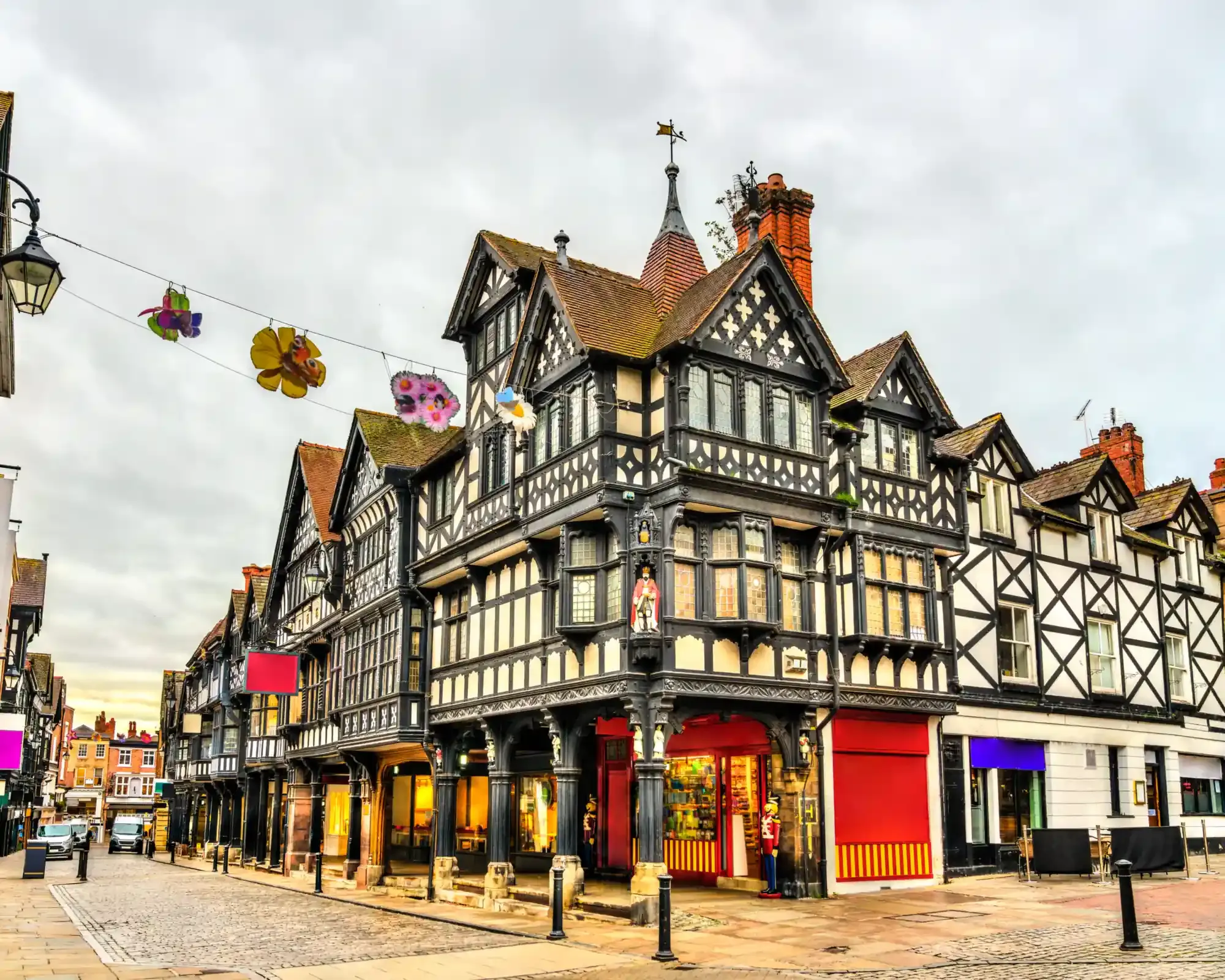 Black-and-white timber-framed buildings of the Chester Rows on a cobbled street in Chester city centre.