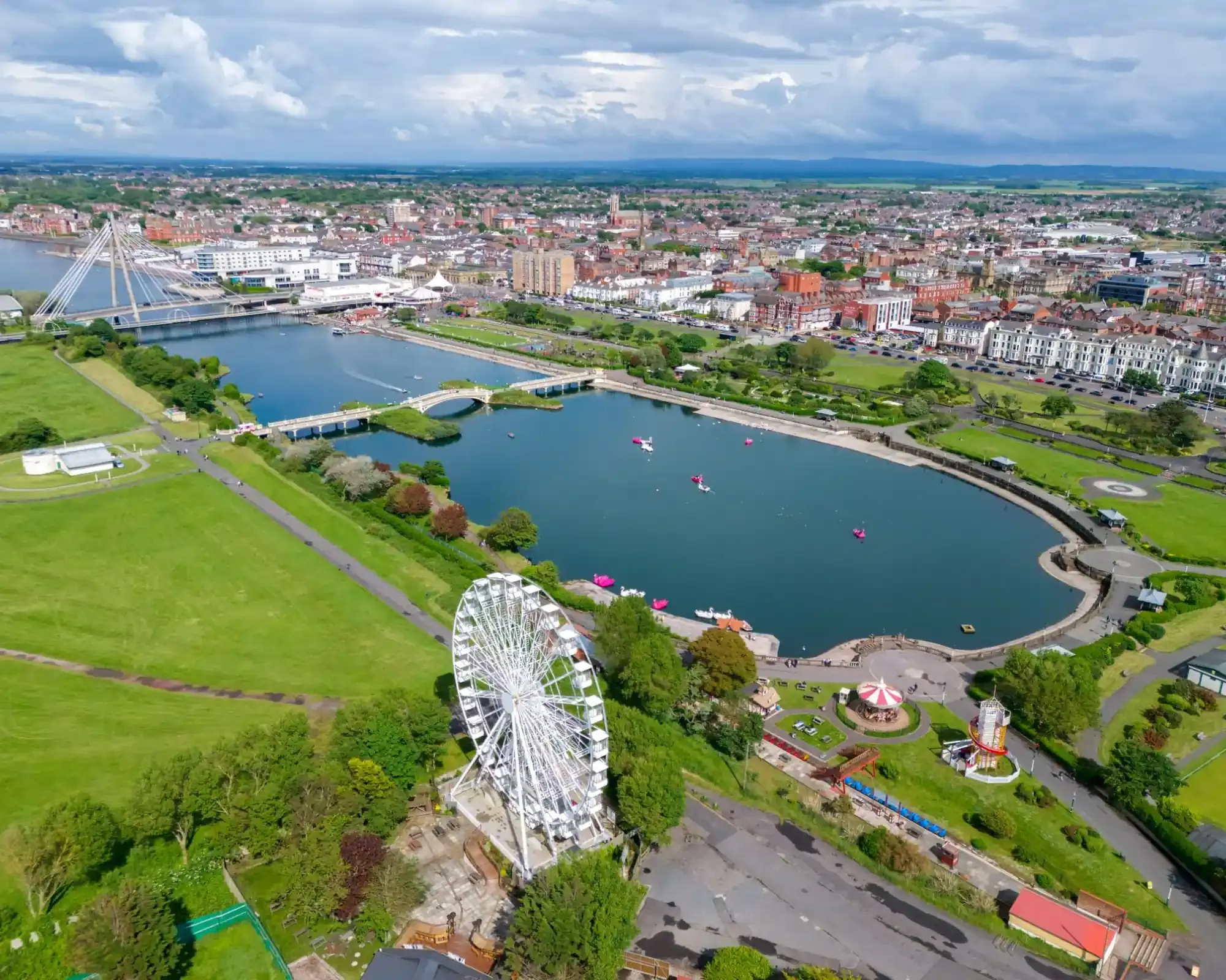 Aerial view of Southport's Marine Lake and King's Gardens, with the Marine Way bridge, a big wheel and the town centre beyond.