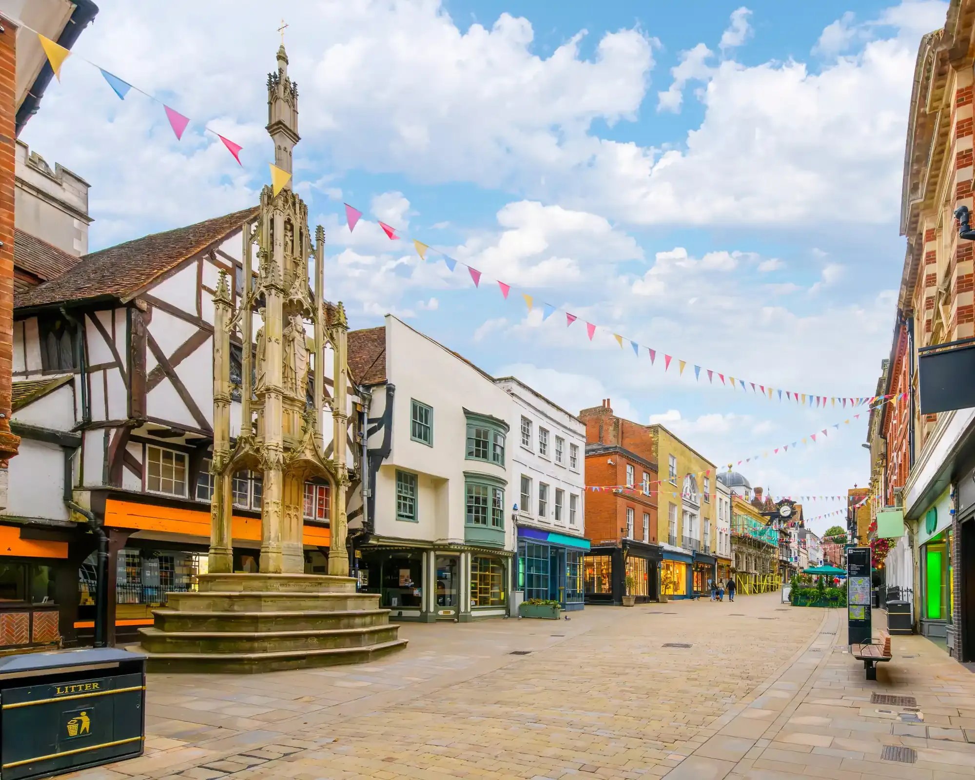 The medieval Buttercross on Winchester High Street, with timber-framed and Georgian shopfronts under colourful bunting.