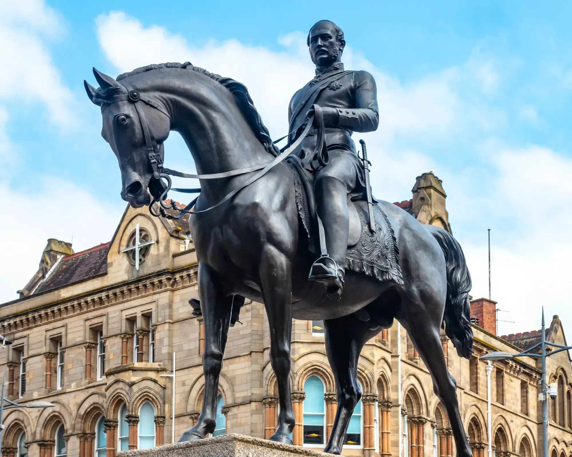 The bronze equestrian statue of Prince Albert in Queen Square, Wolverhampton, in front of a Victorian sandstone building.