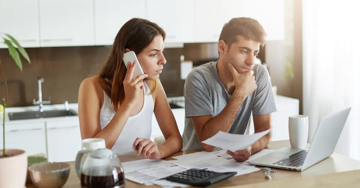 Couple at a kitchen table going through mortgage paperwork with a calculator and laptop