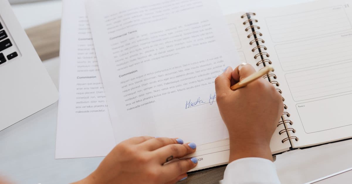 Close-up of hands signing a contract on a desk with office supplies, symbolizing legal agreements.