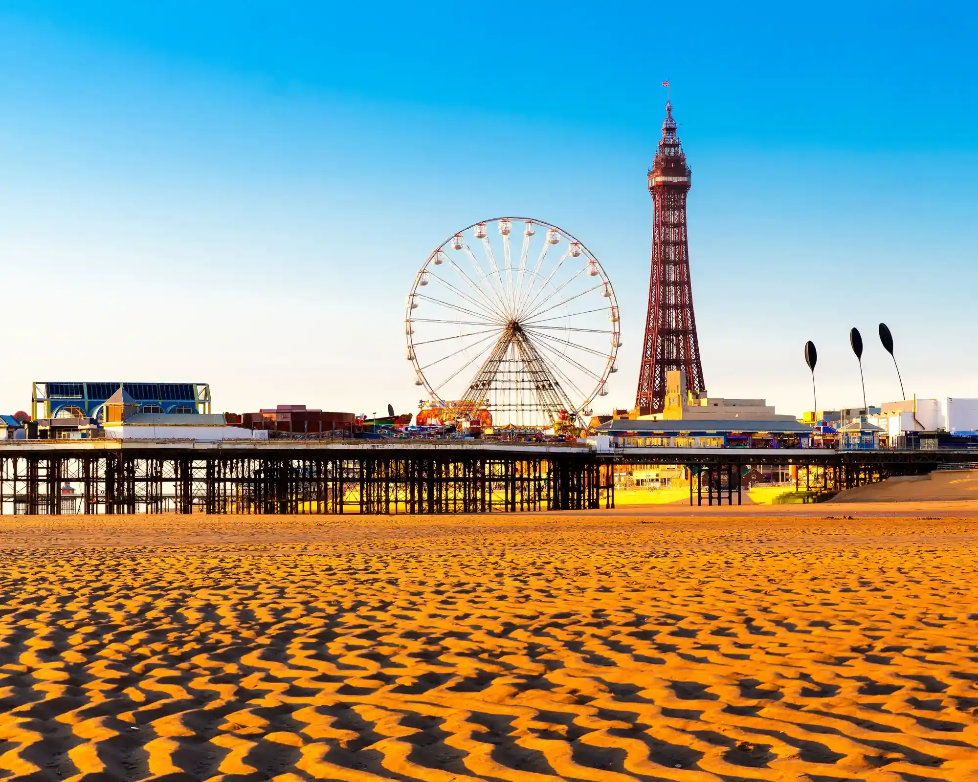 Blackpool Tower and the big wheel on Central Pier seen across rippled sand on Blackpool beach at golden hour.