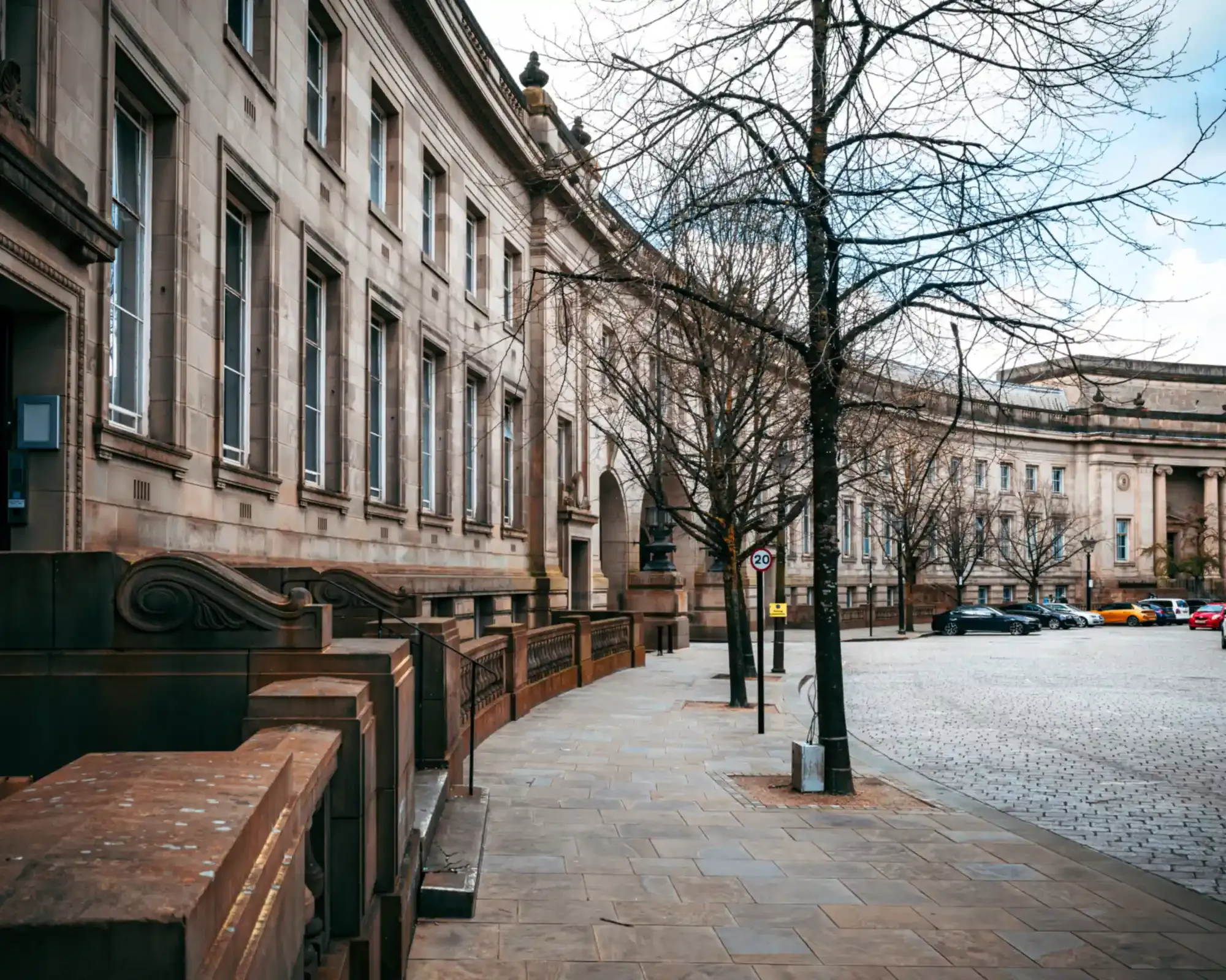 The curved sandstone civic buildings of Le Mans Crescent in Bolton town centre, with bare trees along a cobbled street.