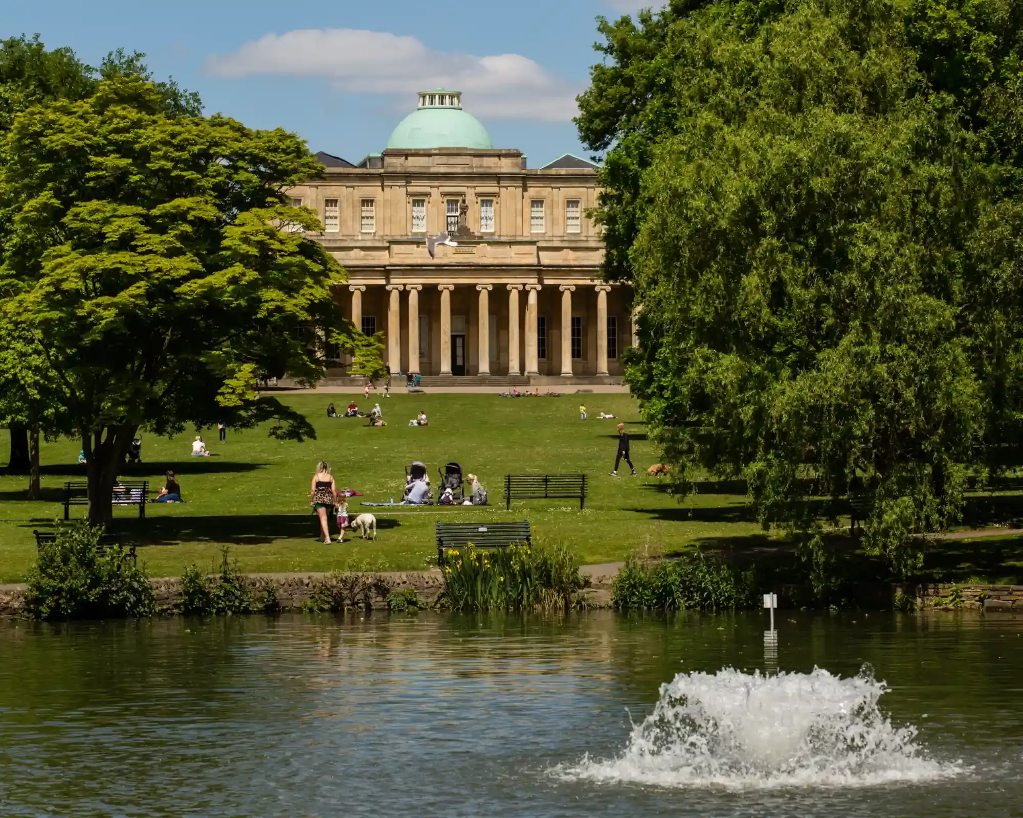 Pittville Pump Room in Cheltenham, seen across the lake in Pittville Park on a sunny day.