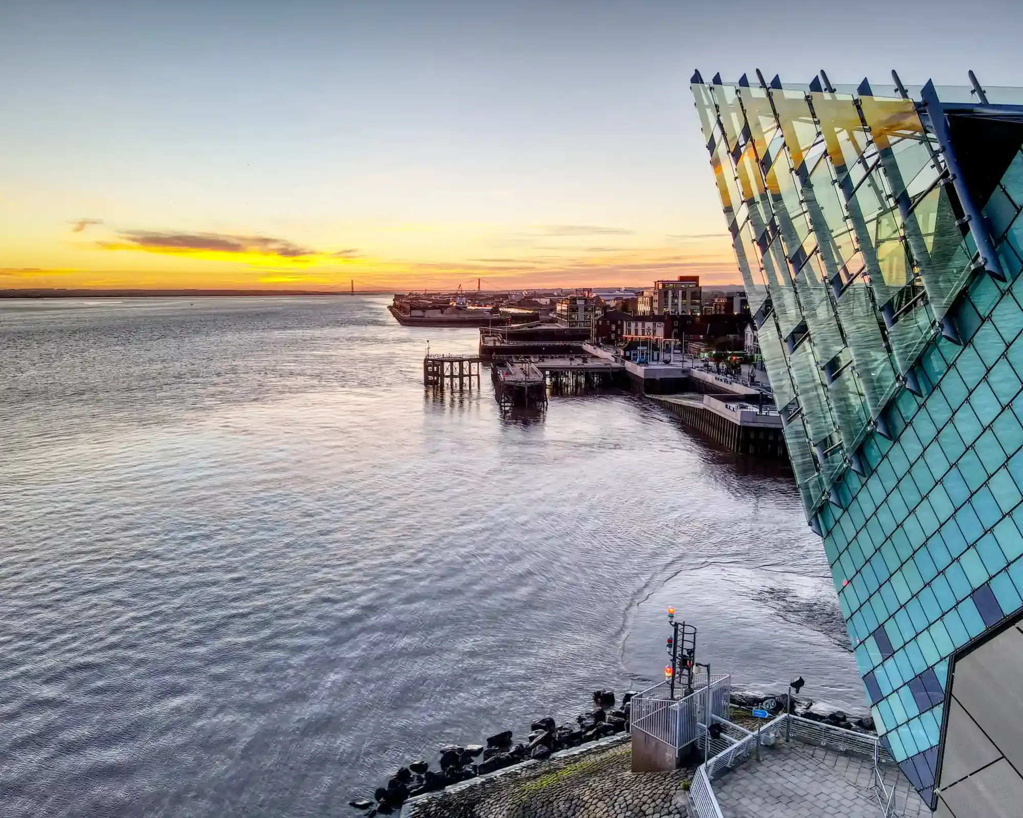 The Deep aquarium beside the Humber Estuary at sunset in Hull, with the Humber Bridge on the horizon.