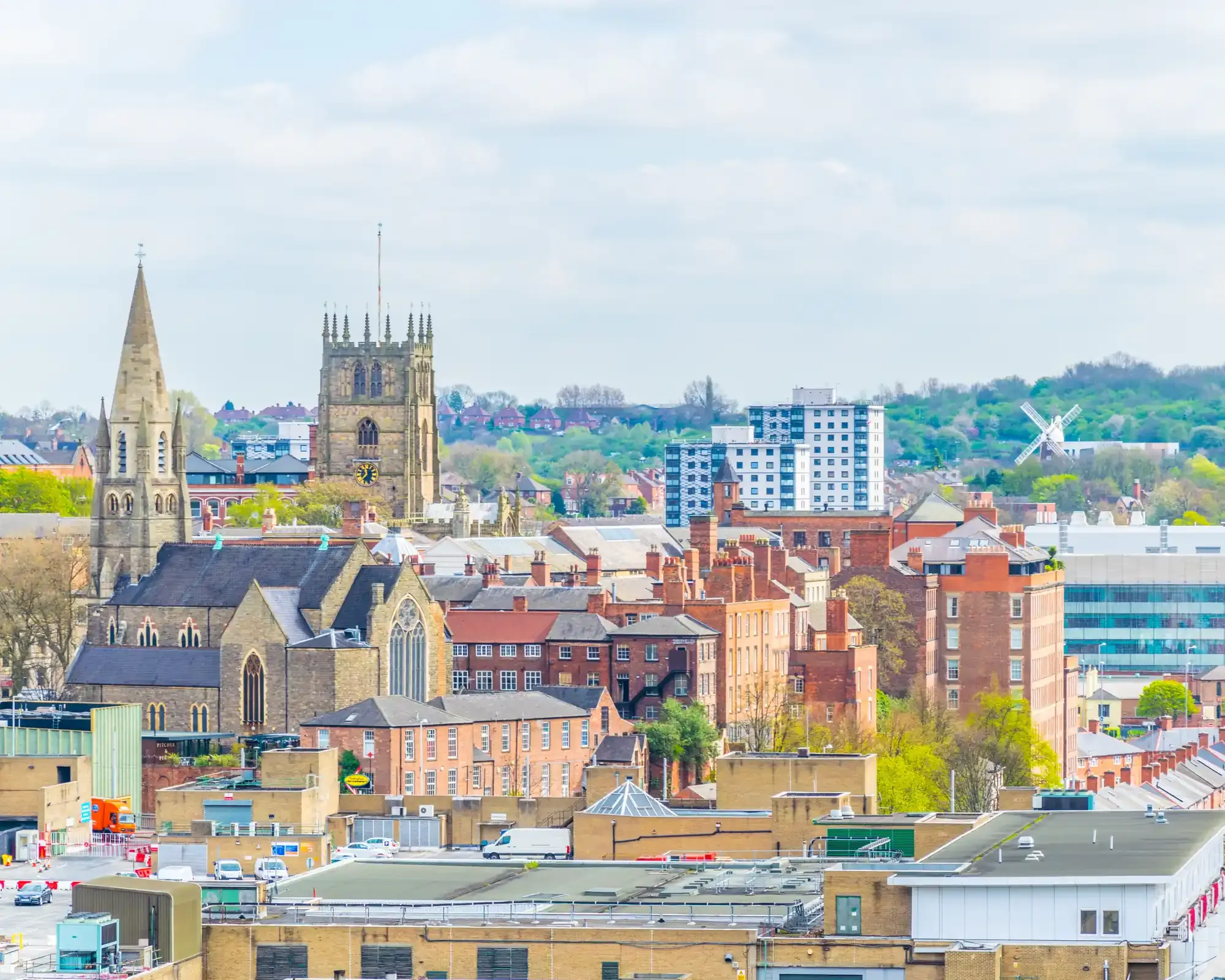 Nottingham's Lace Market skyline, with St Mary's Church tower, a church spire and red-brick buildings, and Green's Windmill on the green hillside beyond.