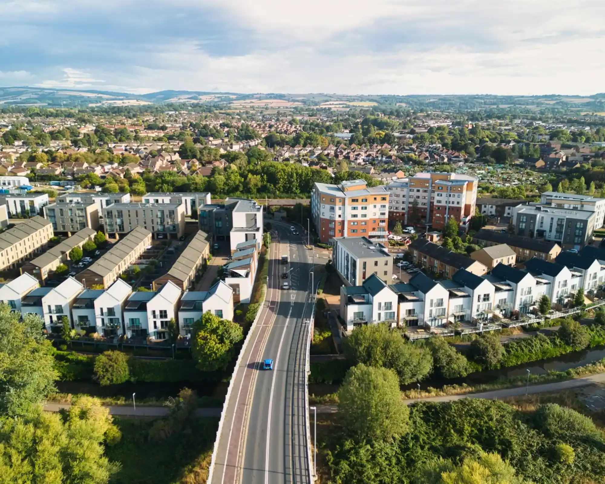 Aerial view of modern townhouses and apartments beside the waterside path in Taunton, with hills beyond.