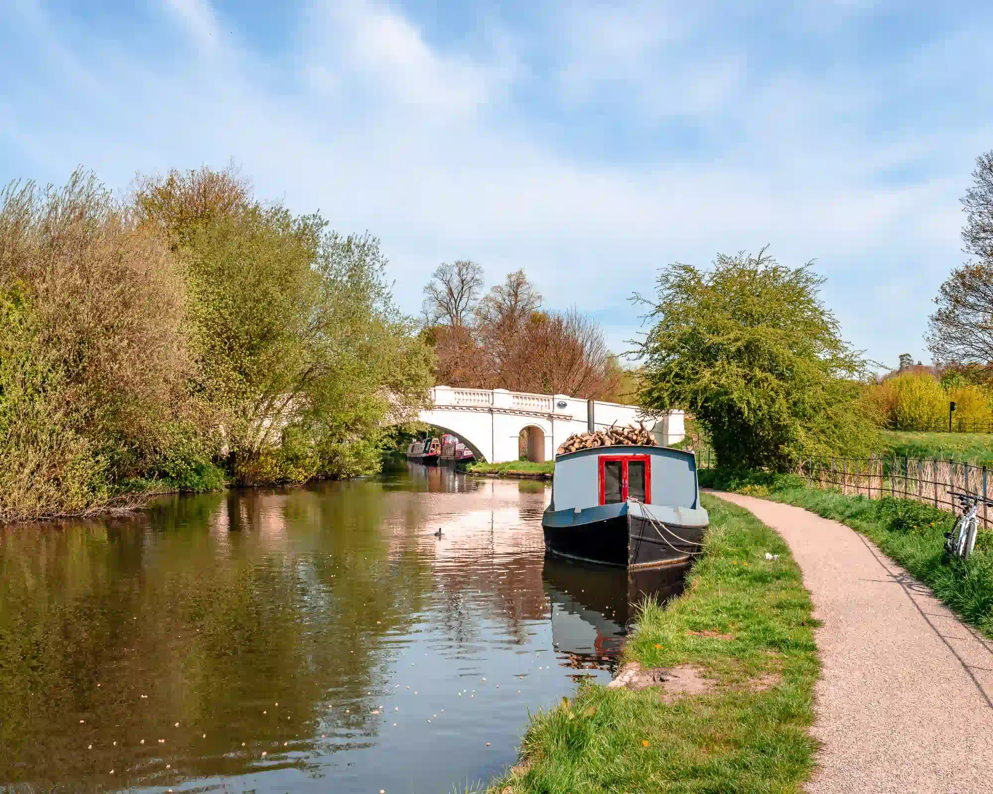 A narrowboat moored on the River Gade, part of the Grand Union Canal, beside the ornate white Grove Bridge in Cassiobury Park, Watford.